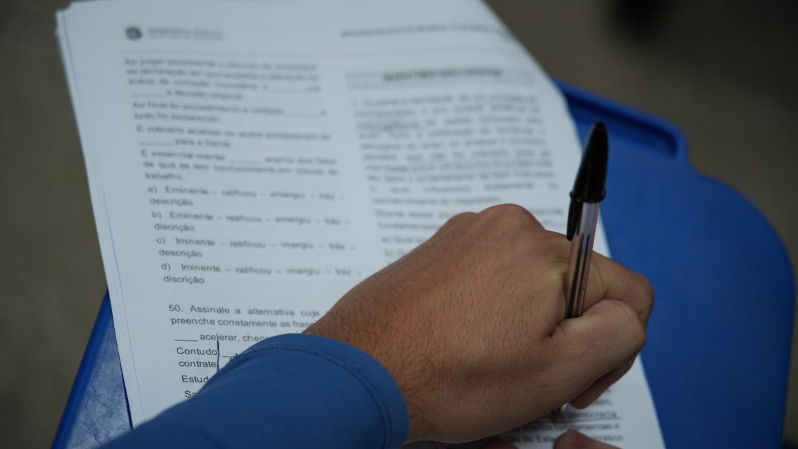 Uma pessoa com uma prova de avaliação em mãos e uma caneta respondendo uma prova