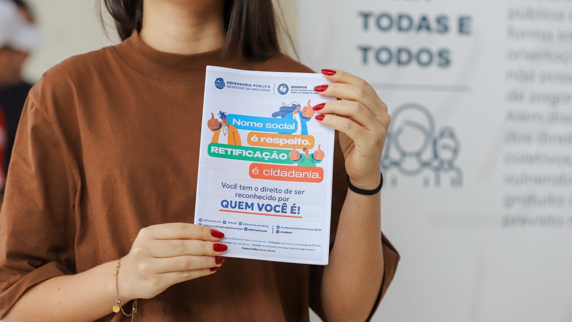 Na foto vemos uma pessoa com camisa marrom e cabelos compridos segurando a cartilha