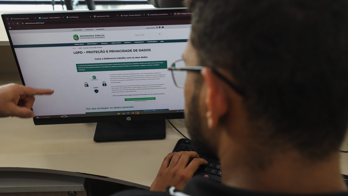Na imagem vemos uma tela de computador aberta no site da Defensoria, na aba da LGPD, e uma pessoa lendo