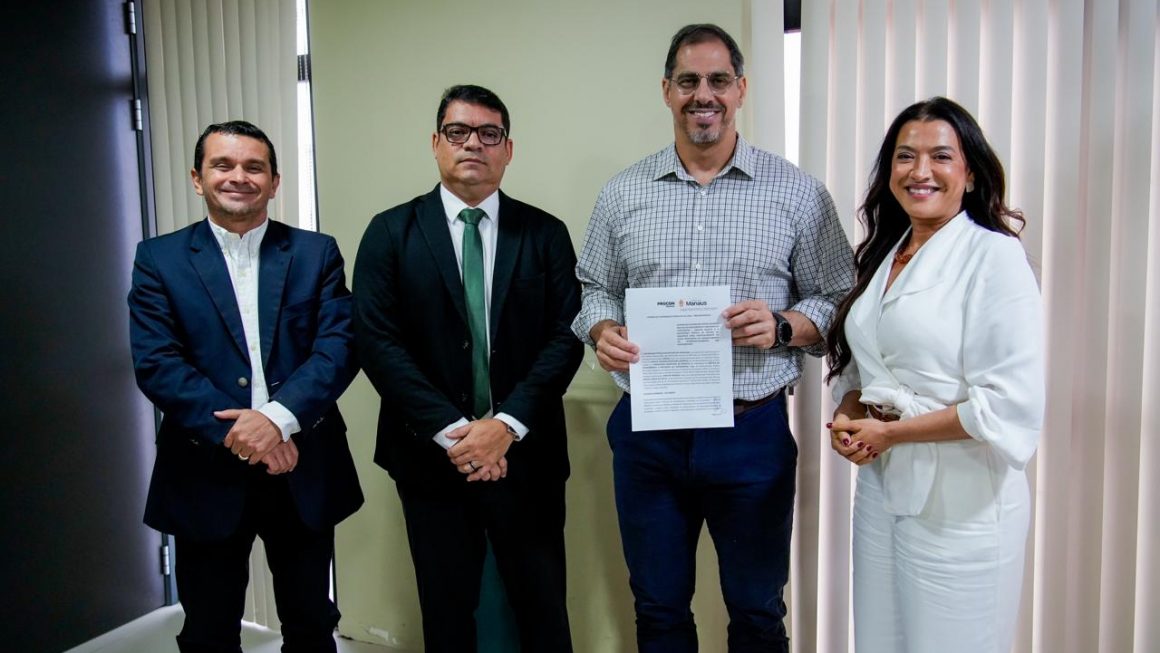 Três defensores e presidente do procon posam de pé para a a fotografia. O defensor público geral segura o termo de acordo