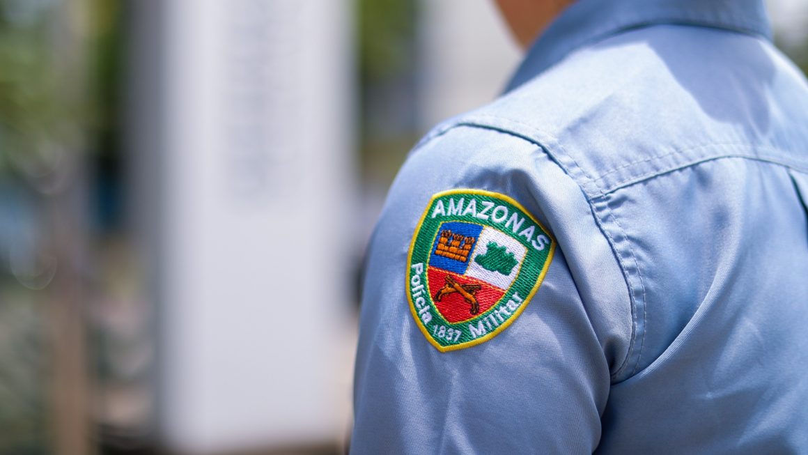 Na imagem, vemos uma policial militar, sem identificar o rosto, de costas, em frente à sede da Defensoria