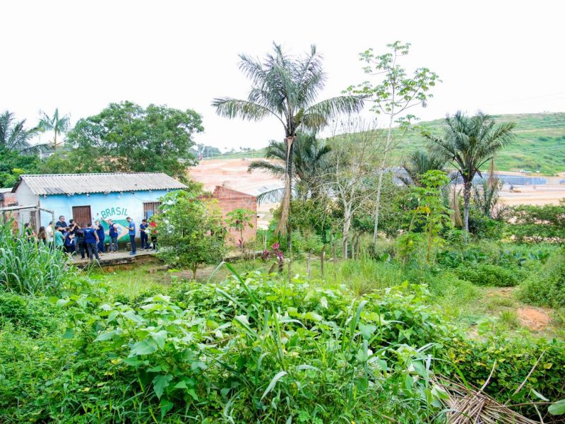 A foto mostra um terreno vizinho ao aterro municipal, que aparece ao fundo, cheio de pessoas das equipes da Defensoria e do gabinete do deputado Amom Mandel, além de comunitários