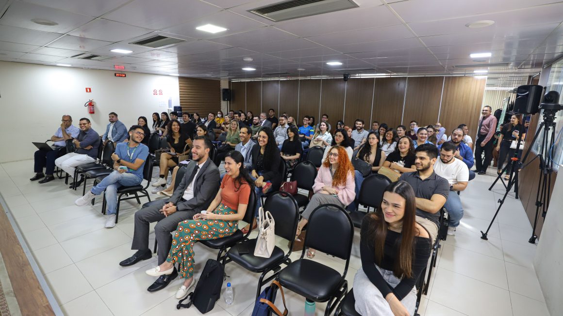 A imagem mostra o auditório da DPE-AM, com as pessoas sentadas assistindo a uma palestra