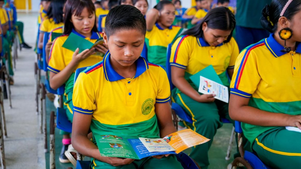 Estudante indígena lê folder dos projetos Defensoria nas Escolas e Caminhos da Inclusão