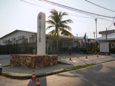 A imagem mostra a fachada do prédio da Casa da Cidadania, com um totem identificador da DPE-AM, com nome e logomarca da instituição, na frente do prédio