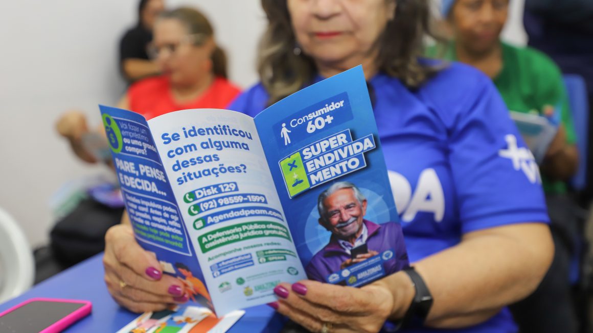 Idosa lê folder com orientações sobre direitos do consumidor