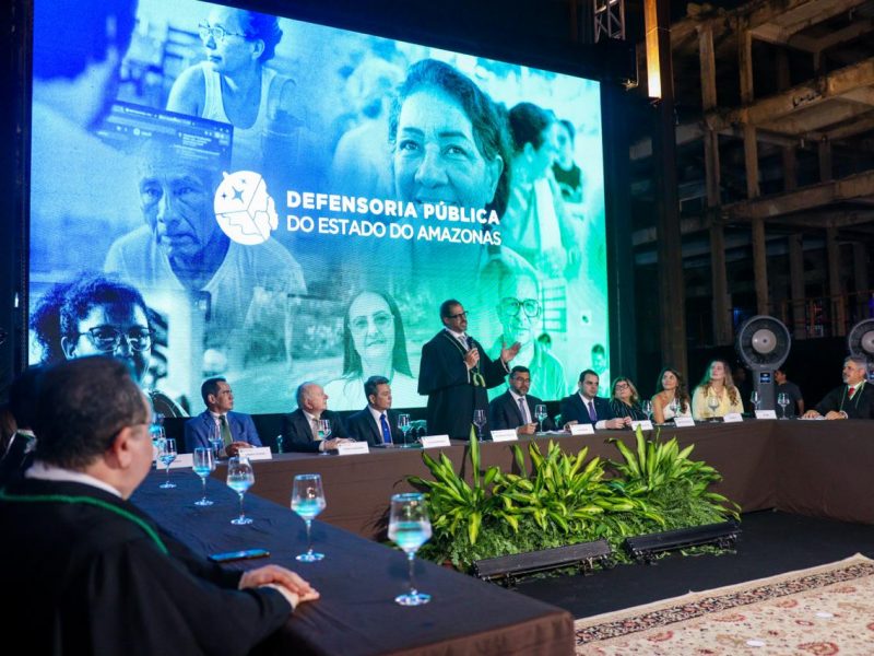 Imagem mostra a mesa de autoridades durante a posse, com o defensor geral em pé ao centro, com microfone na mão