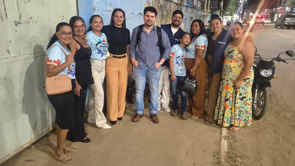 A imagem mostra mães associadas e o defensor Renato Fernandes ao centro, em foto posada, com todos de pé