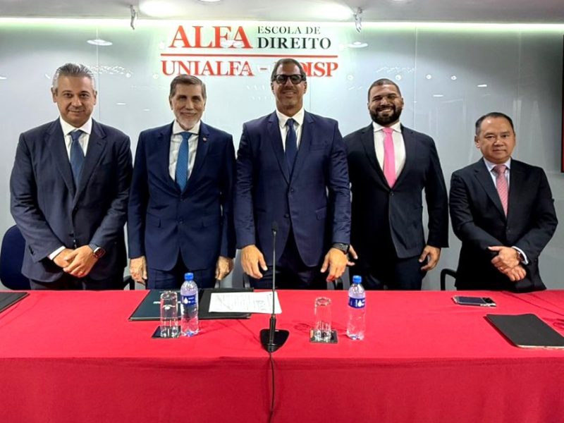 A imagem mostra os defensores do Amazonas e o reitor da Fadisp de pé, todos de terno, posando para foto atrás de uma mesa vermelha; ao fundo vemos uma placa com o nome da universidade
