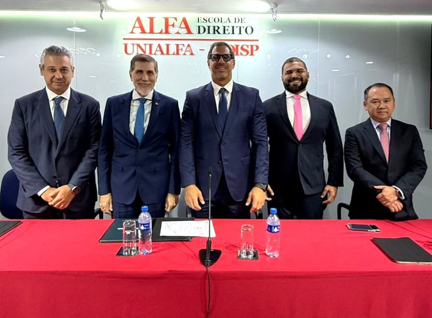 A imagem mostra os defensores do Amazonas e o reitor da Fadisp de pé, todos de terno, posando para foto atrás de uma mesa vermelha; ao fundo vemos uma placa com o nome da universidade