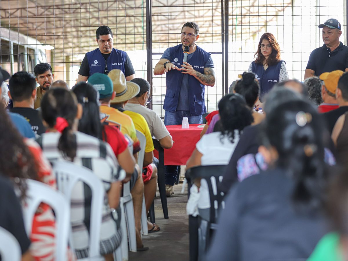 Na imagem vemos o defensor Carlos Almeida e assessores da DPE-AM em pé, atrás de uma mesa, falando para os agricultores, que estão à frente, sentados em cadeiras plásticas