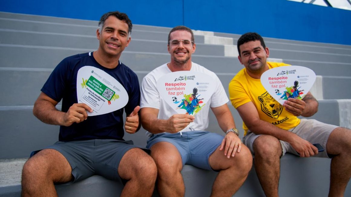Três pais na arquibancada segurando ventarolas da campanha Jogo Limpo