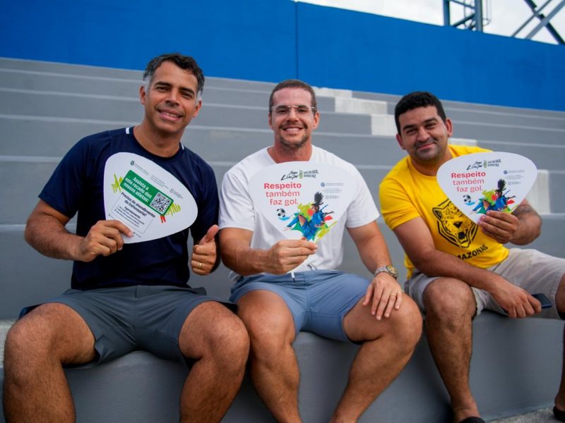 Três pais na arquibancada segurando ventarolas da campanha Jogo Limpo